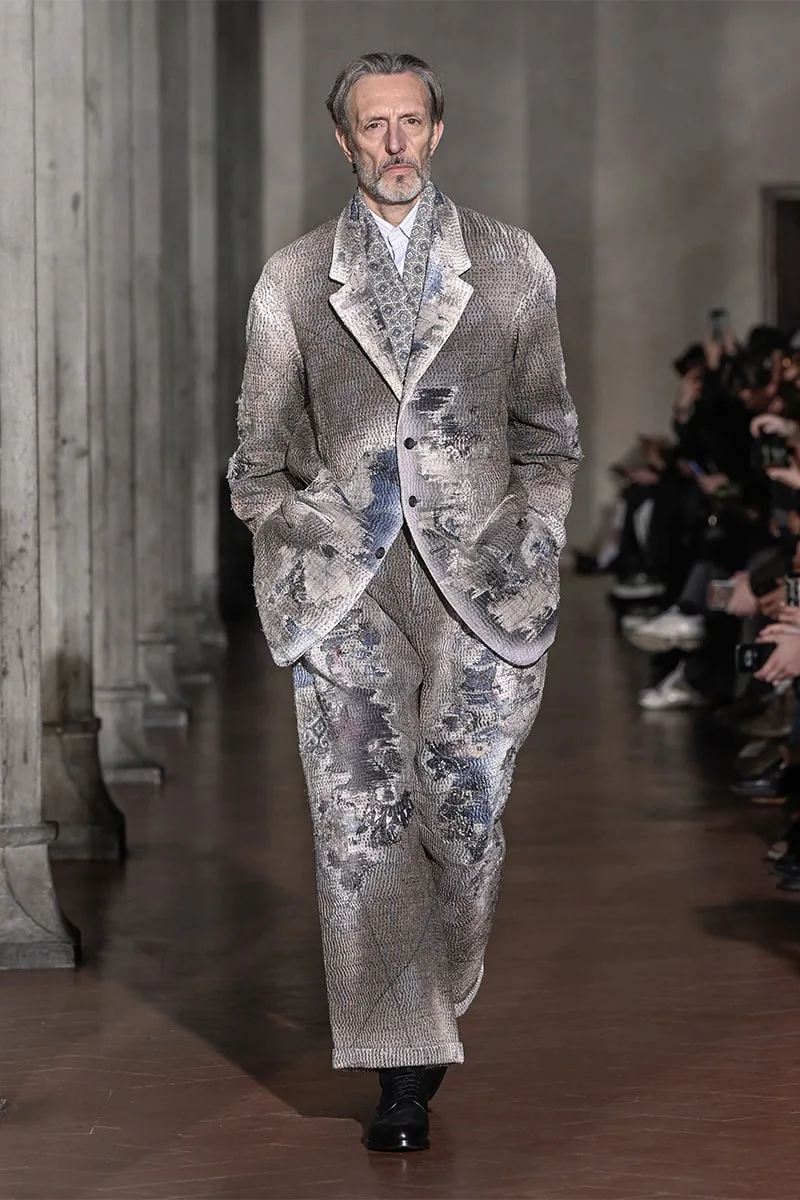 Homme défilant en costume texturé, ambiance élégante et classique.