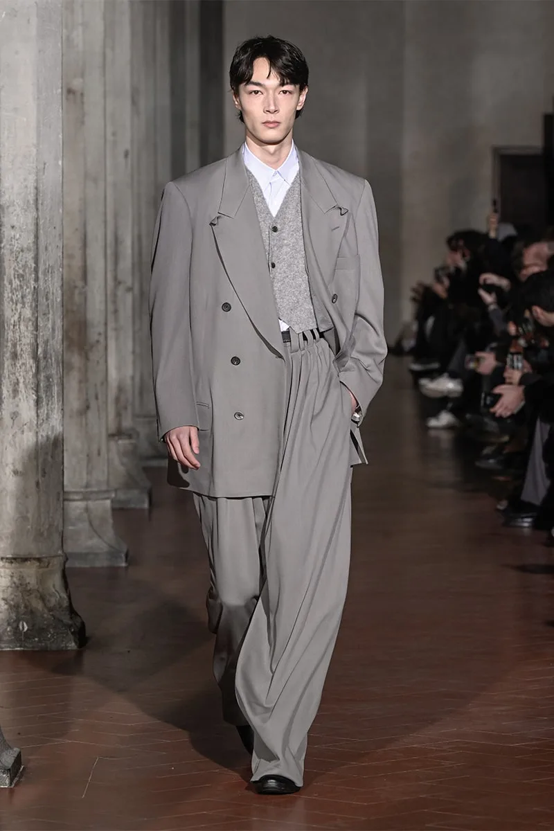 Homme défilant en costume large gris sur un podium.