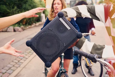 Trois personnes échangent un haut-parleur portable dehors en vélo.