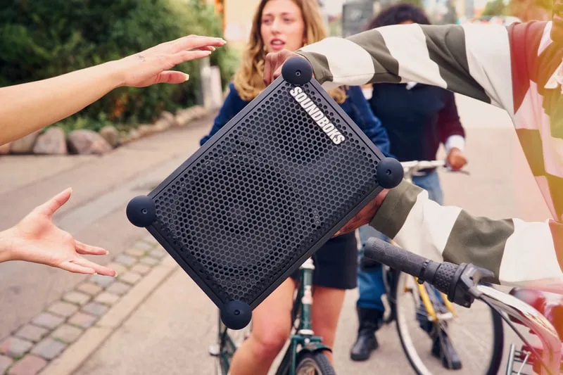 Trois personnes échangent un haut-parleur portable dehors en vélo.