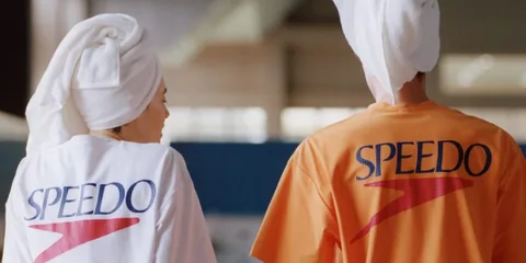 Deux personnes portant des t-shirts Speedo avec serviettes blanches sur la tête.