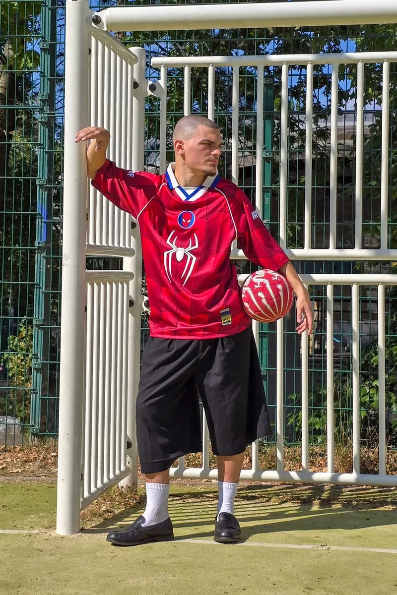 Homme avec maillot rouge Spider-Man et ballon sur un terrain de sport.