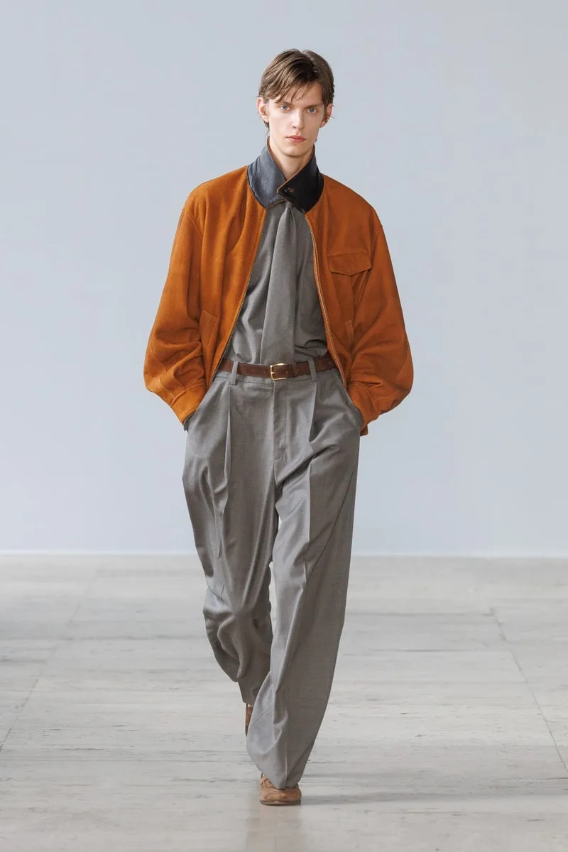 Homme défilant en veste marron et pantalon gris élégant.