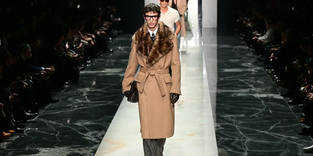 Défilé de mode homme avec manteau long et fourrure, sol marbré.