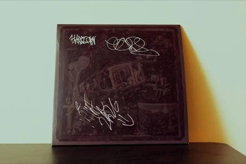 Pochette d'album avec des signatures artistiques blanches.