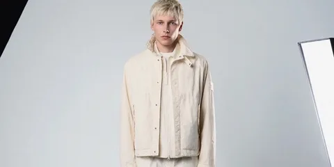 Homme en veste beige sur fond clair, ambiance studio.