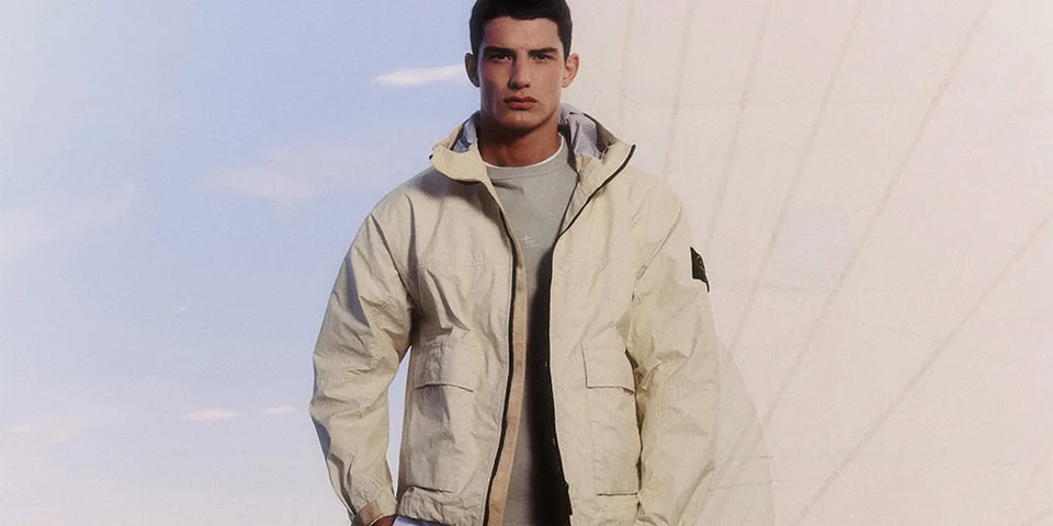 Homme en veste beige devant un ciel bleu et structure moderne.