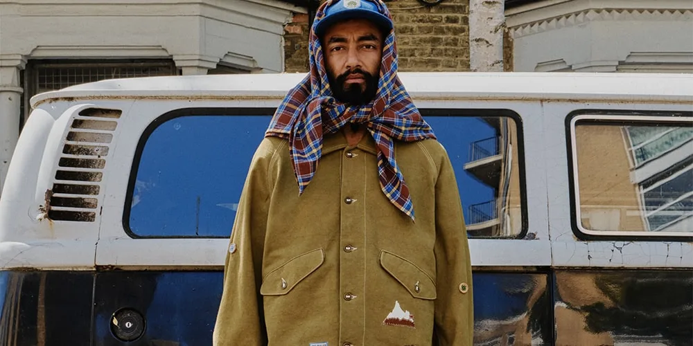 Homme devant une camionnette, portant une tenue unique et un foulard à carreaux.