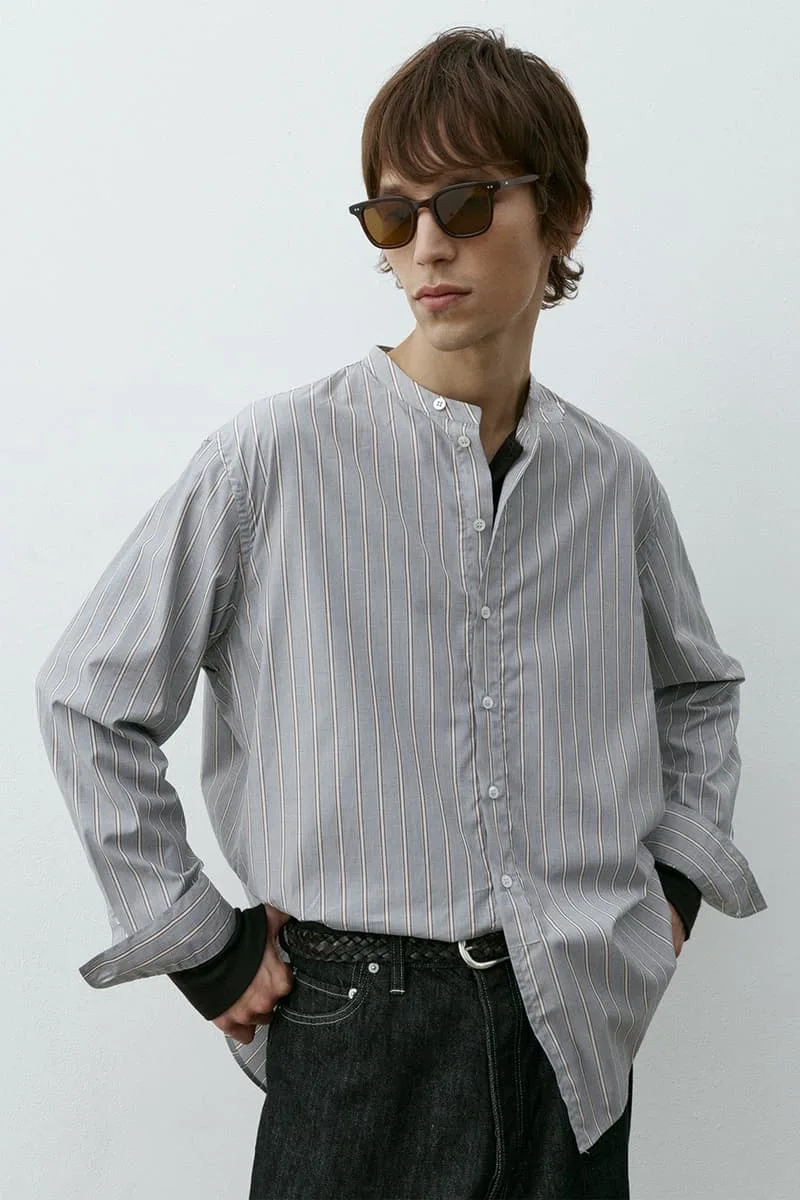 Homme avec chemise rayée, lunettes de soleil, pose décontractée.