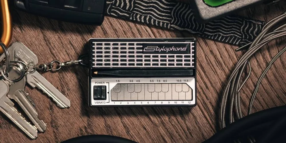 Petit synthétiseur noir Stylophone avec clés et câbles sur table en bois.