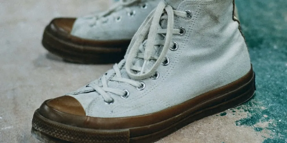 Chaussures montantes blanches avec semelle et bout marron sur fond de béton.