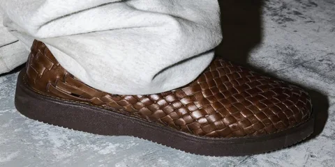 Chaussure marron tressée avec pantalon clair sur sol gris.