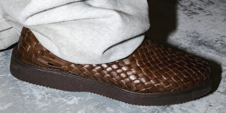 Chaussure marron tressée avec pantalon clair sur sol gris.