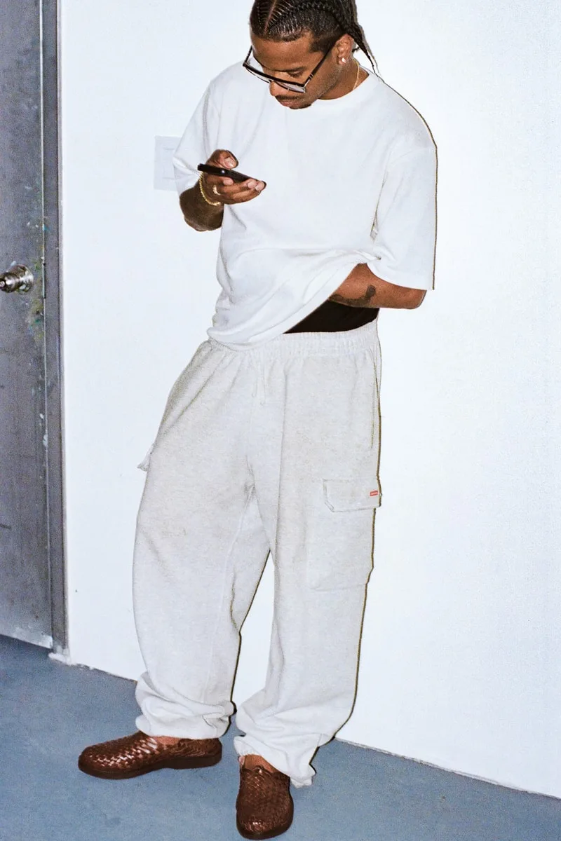 Homme avec t-shirt blanc et pantalon gris regarde son téléphone.