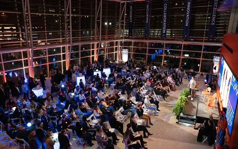 Public réunis dans une salle de conférence pour écouter une présentation sur scène.