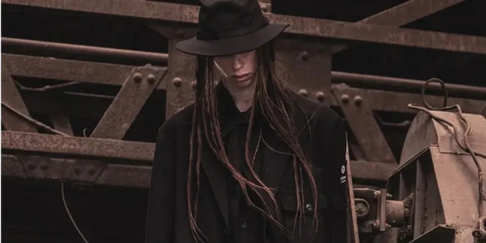 Personne en noir avec un chapeau dans un cadre industriel.