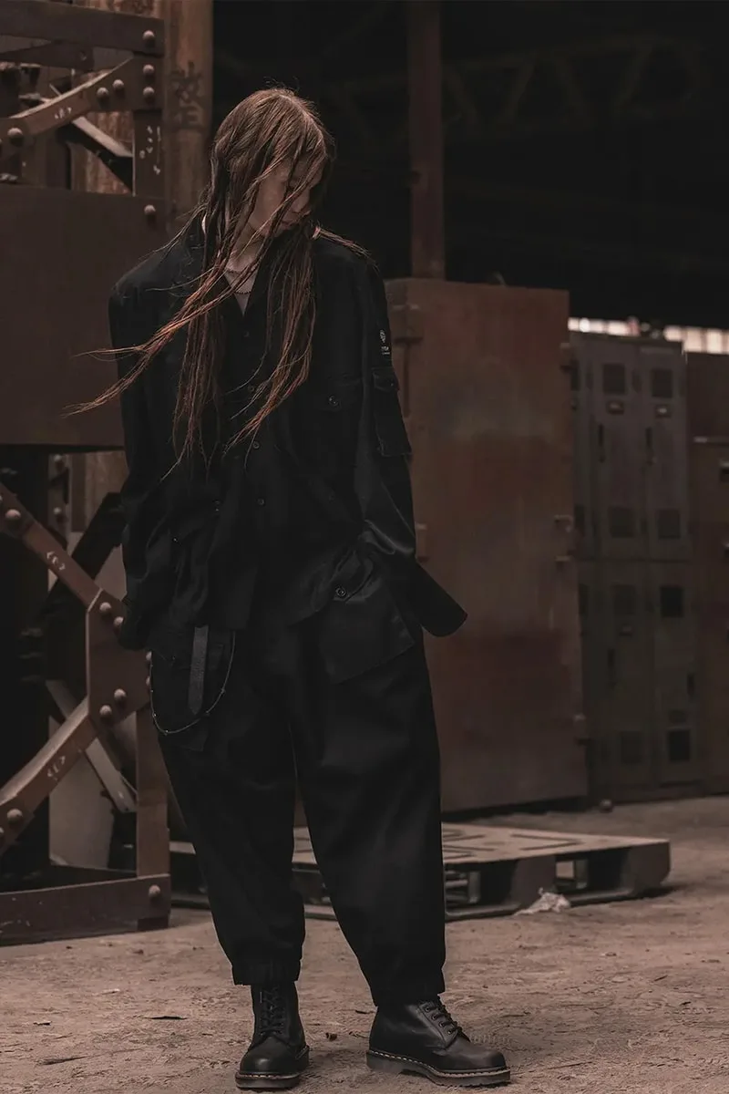 Personne en tenue noire avec cheveux longs dans un cadre industriel.