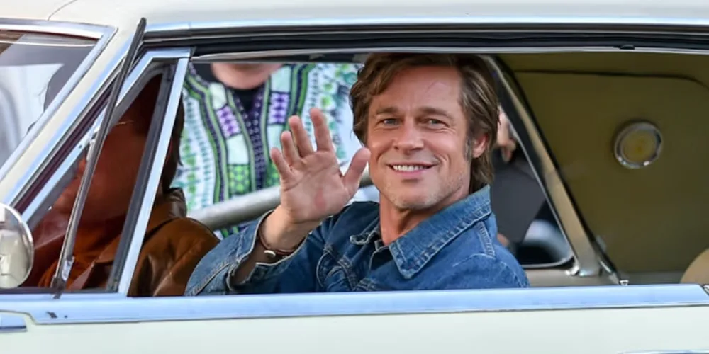 Homme souriant en jean dans une voiture, saluant par la fenêtre.