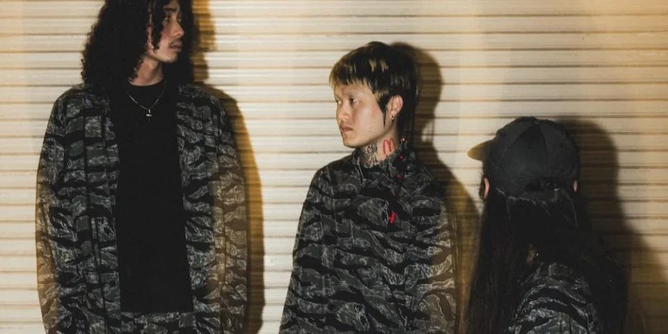Trois personnes dans des vêtements camouflés devant un mur.