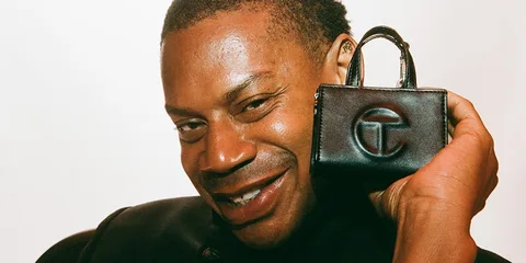 Homme souriant tenant un petit sac noir avec logo.