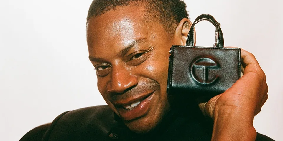 Homme souriant tenant un petit sac noir avec logo.