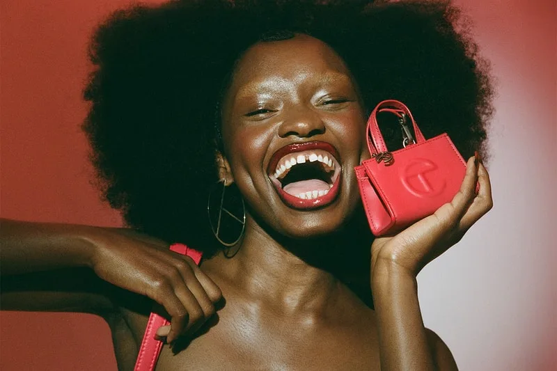 Femme souriante avec un petit sac rose vif, fond rouge.