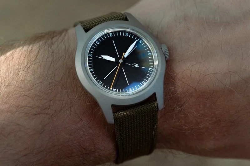 Montre-bracelet sur poignet avec cadran noir et bracelet en toile.
