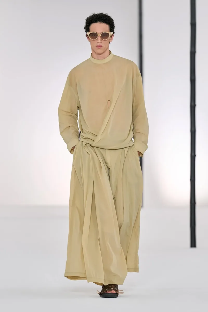 Homme en vêtements beige avec lunettes de soleil sur un podium.