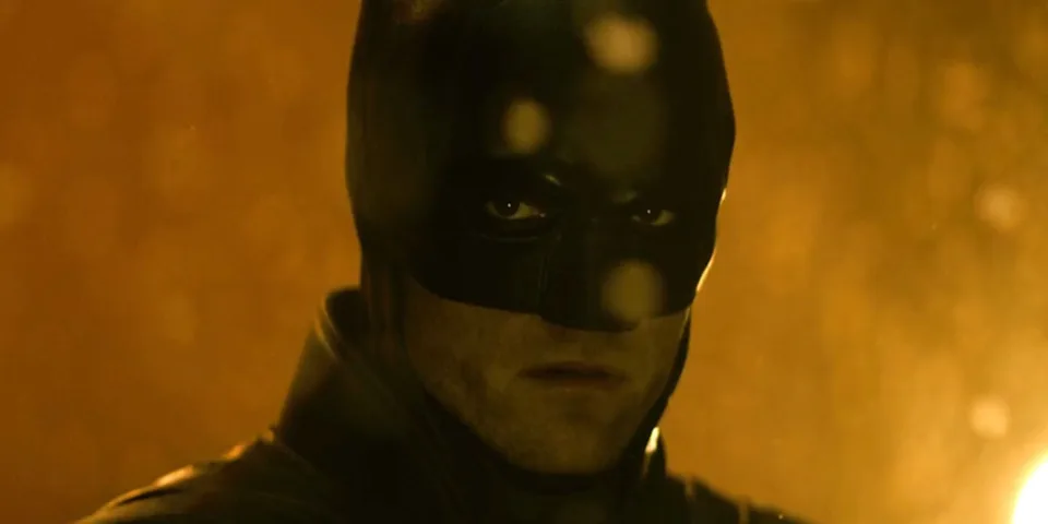 Batman regarde intensément dans une scène sombre et orangée.