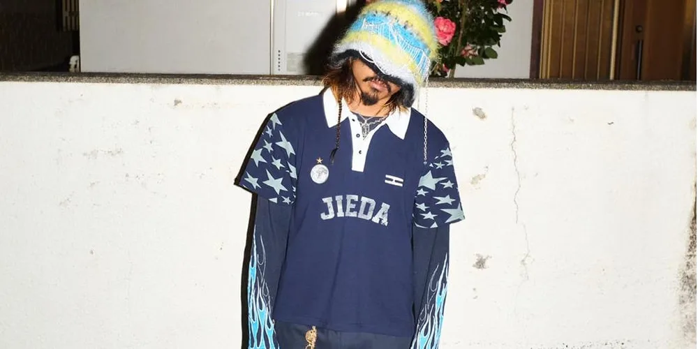 Personne portant un pull bleu avec une casquette, debout devant un mur.