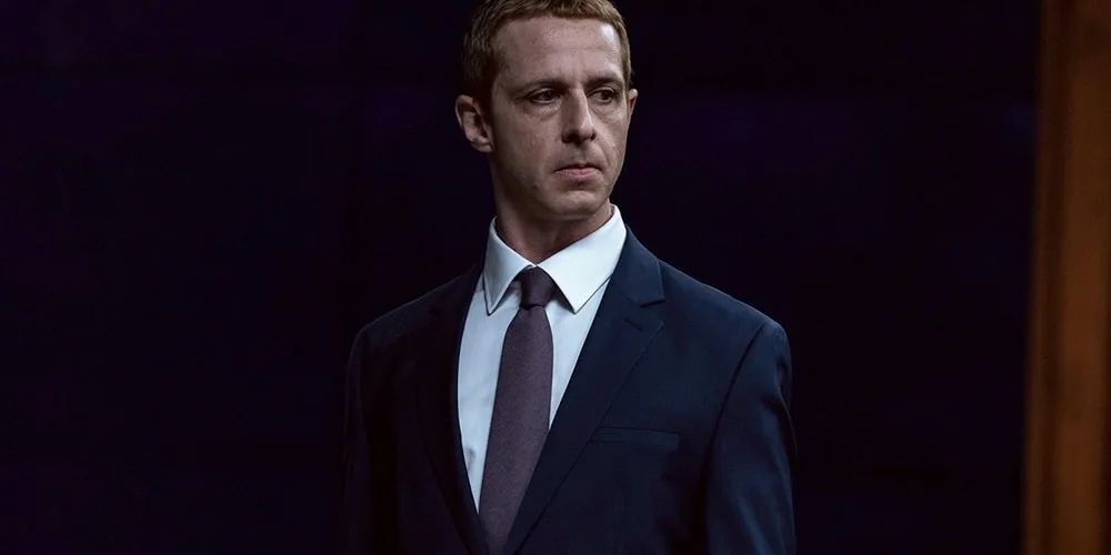 Homme en costume sombre sur fond noir.