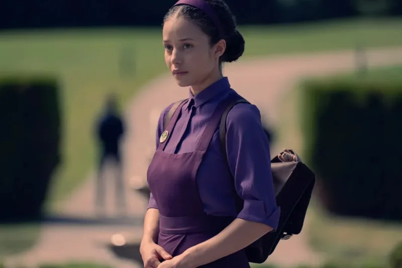 Personne en tenue violette avec un sac à dos devant un parc verdoyant.