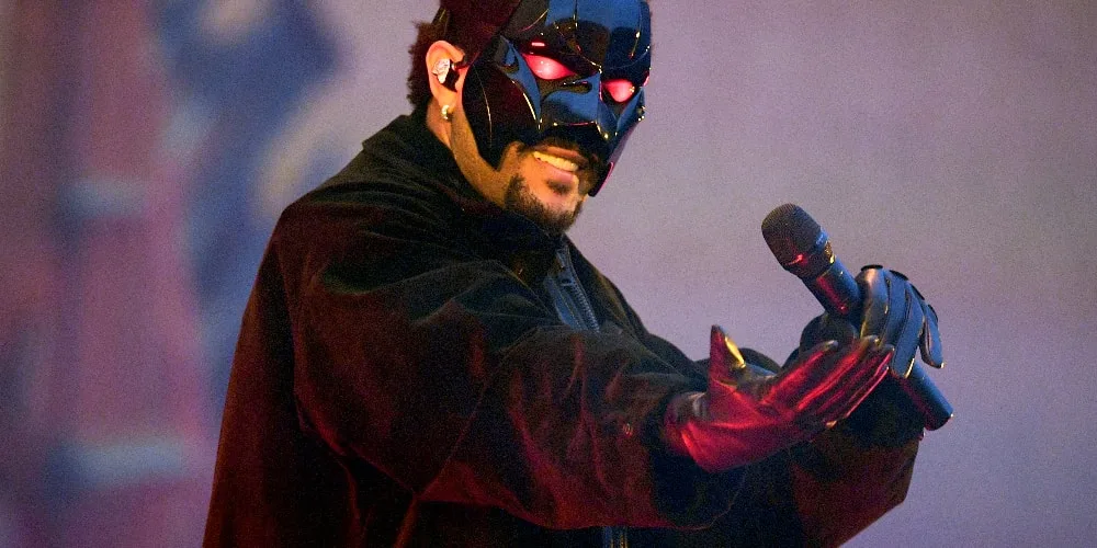 Un chanteur masqué en costume noir tient un micro sur scène.