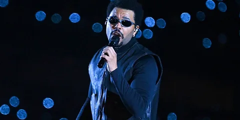 Chanteur avec lunettes de soleil sur scène, fond lumineux.
