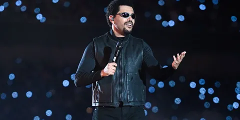 Chanteur avec micro sur scène, lumières en arrière-plan.