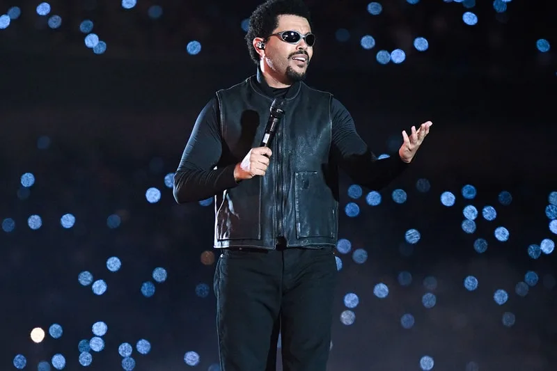 Chanteur sur scène avec des lunettes de soleil et un micro.