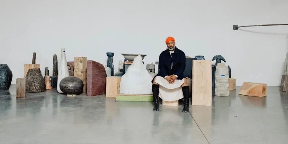 Homme assis entouré de sculptures dans une galerie.
