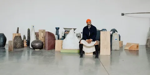 Homme assis entouré de sculptures dans une galerie.