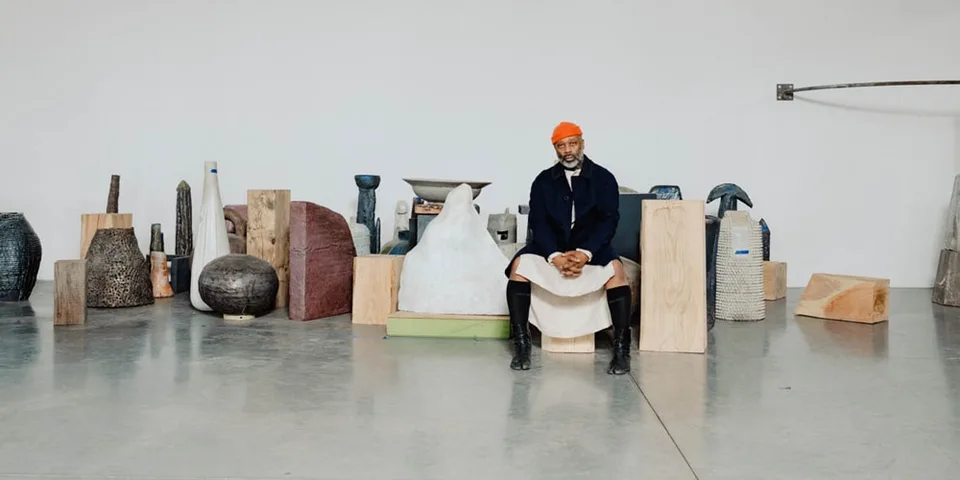 Homme assis entouré de sculptures dans une galerie.