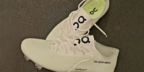Deux chaussures blanches avec un logo 'O' et lacets, posées sur un sol sombre.