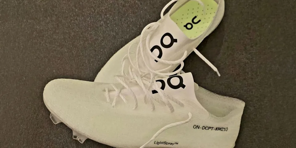 Deux chaussures blanches avec un logo 'O' et lacets, posées sur un sol sombre.