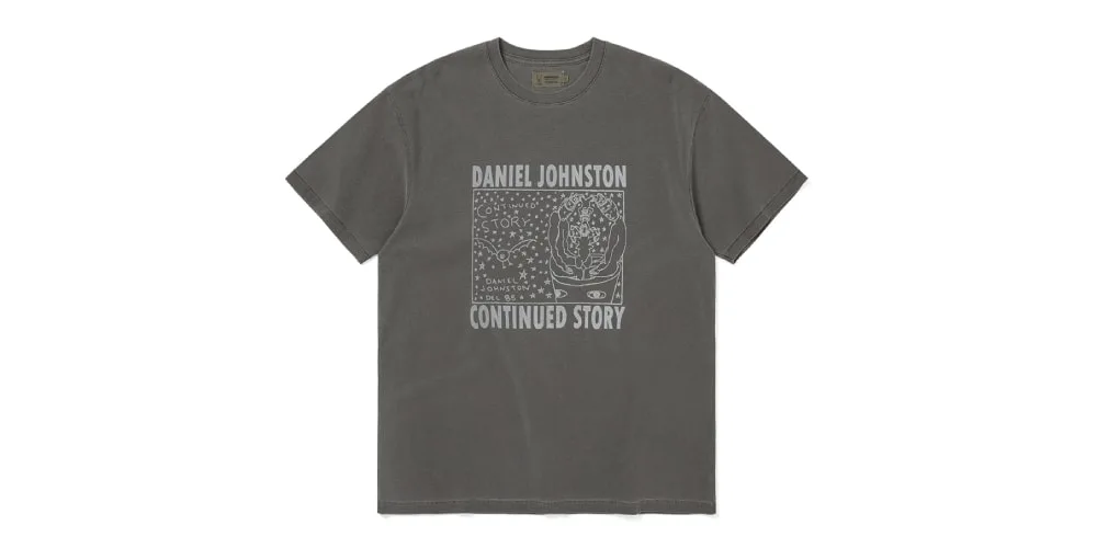 T-shirt gris avec dessin de Daniel Johnston, texte 'Continued Story' en blanc.