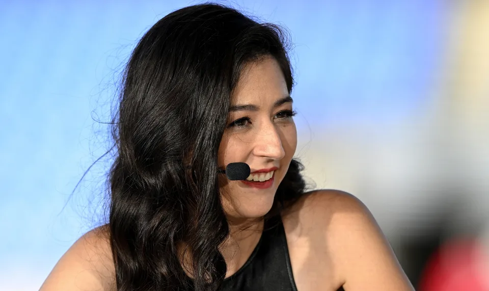 Femme aux cheveux noirs souriant avec un micro-casque sur scène.