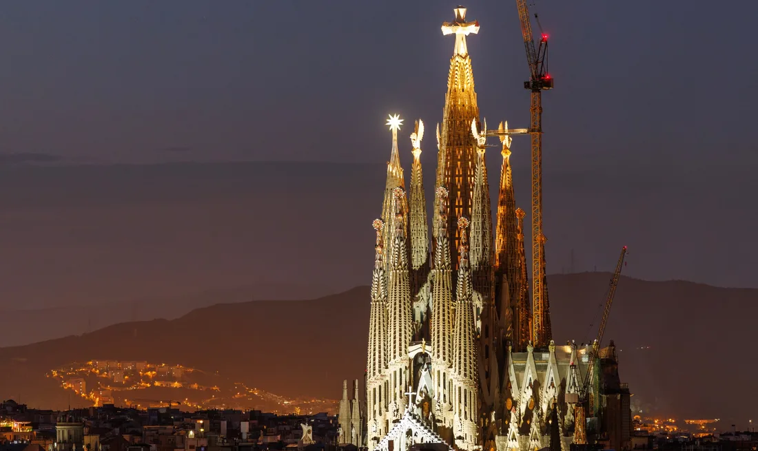Sagrada Família illuminée au crépuscule avec des grues en arrière-plan.