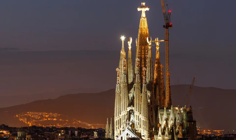 Sagrada Família illuminée au crépuscule avec des grues en arrière-plan.