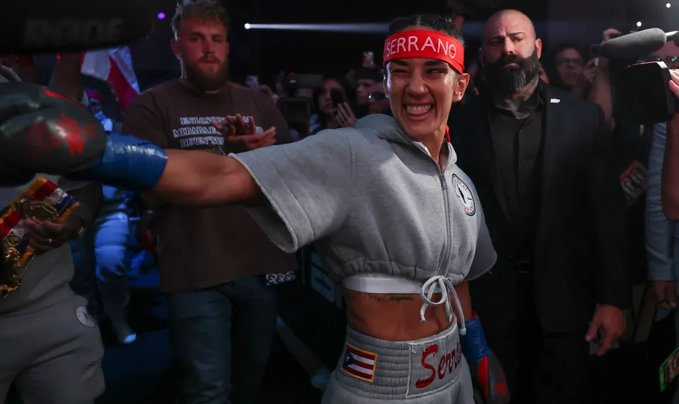 Femme boxeuse souriante avec bandeau rouge entourée de personnes en arrière-plan.