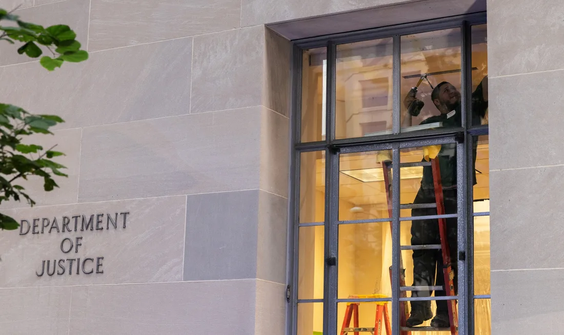 Homme sur une échelle réparant une fenêtre au Department of Justice.