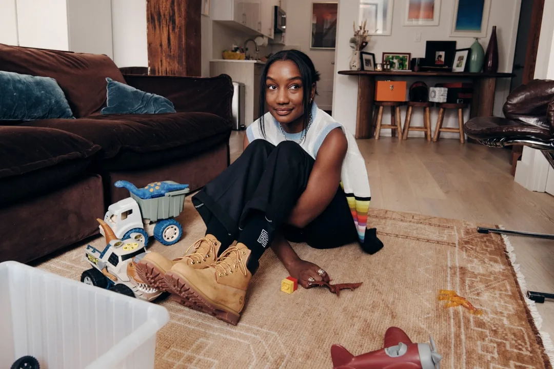 Femme assise jouant avec des jouets sur un tapis dans un salon.