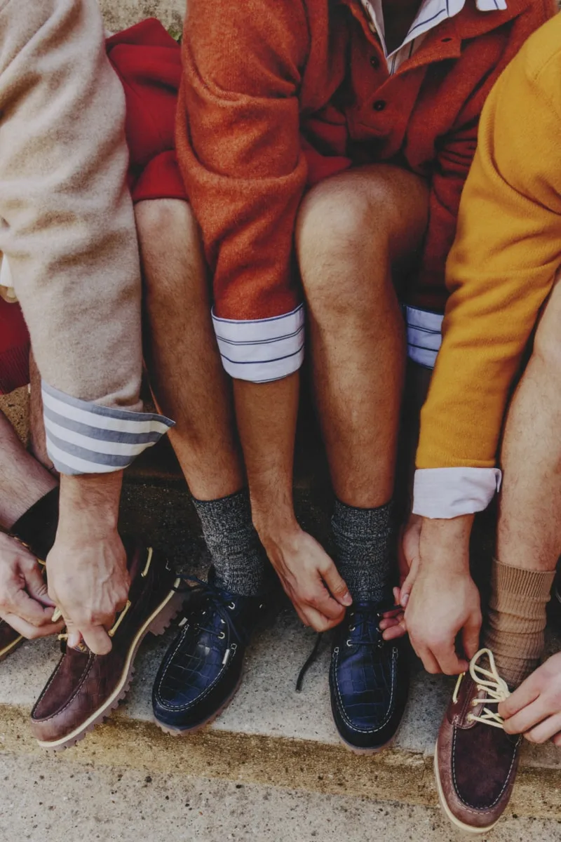 Trois personnes en chemise et pulls, lacent des chaussures en cuir.