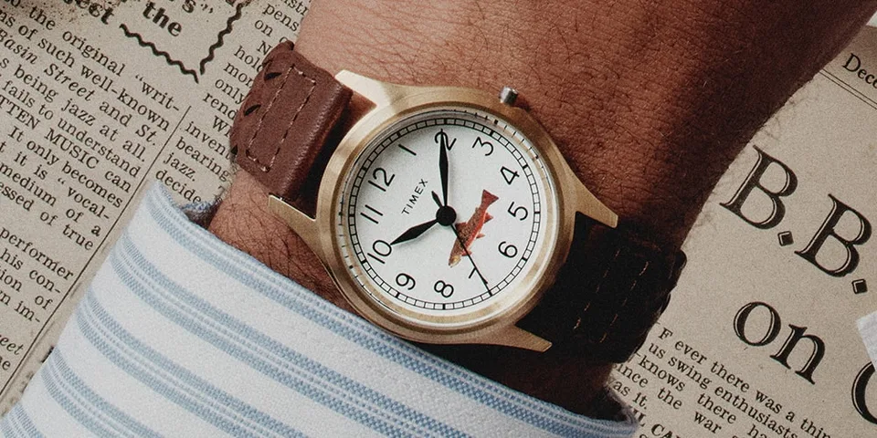 Montre-bracelet marron et fond de journal froissé.